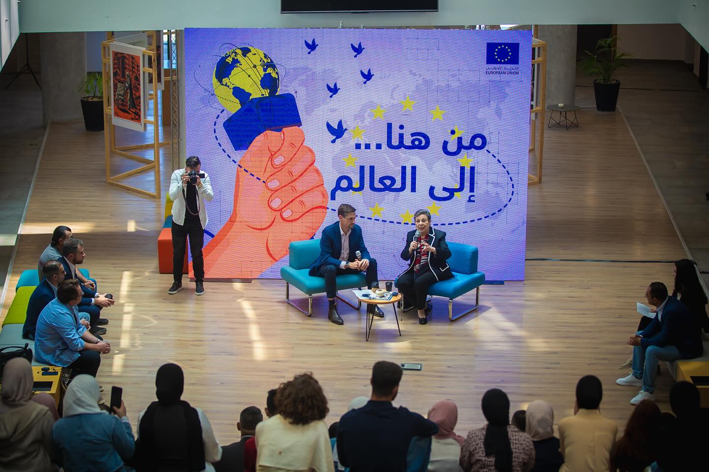 Speakers on stage in front of an event backdrop, with the audience seated below